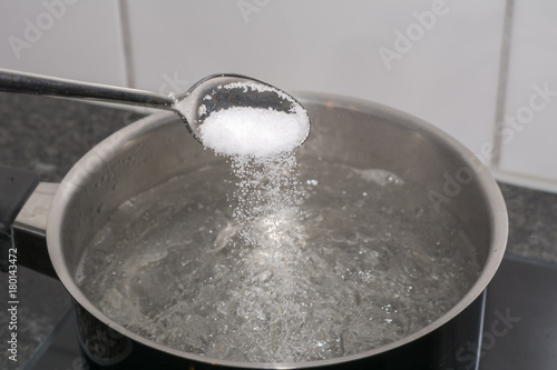 Salz in das kochende Wasser geben mit dem Löffel