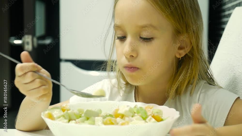 Funny little girl sitting at kitchen table and eating fruit salad from bowl. Funny little girl sitting at kitchen table and eating fruit salad from bowl.