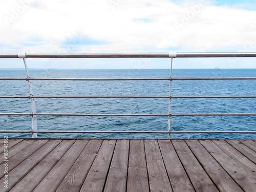 Wooden pier with and steel railings over the sea shore with copy space. Pier at the sea. Sea view from the viewing platform of wooden boards