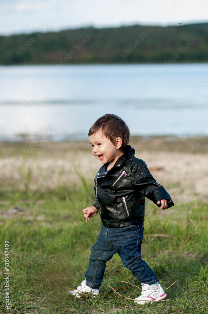 laughing baby girl in a black leather jacket, jeans and a sneaker crouching in the grass laughing baby girl in a black leather jacket, jeans and a sneaker crouching in the grass