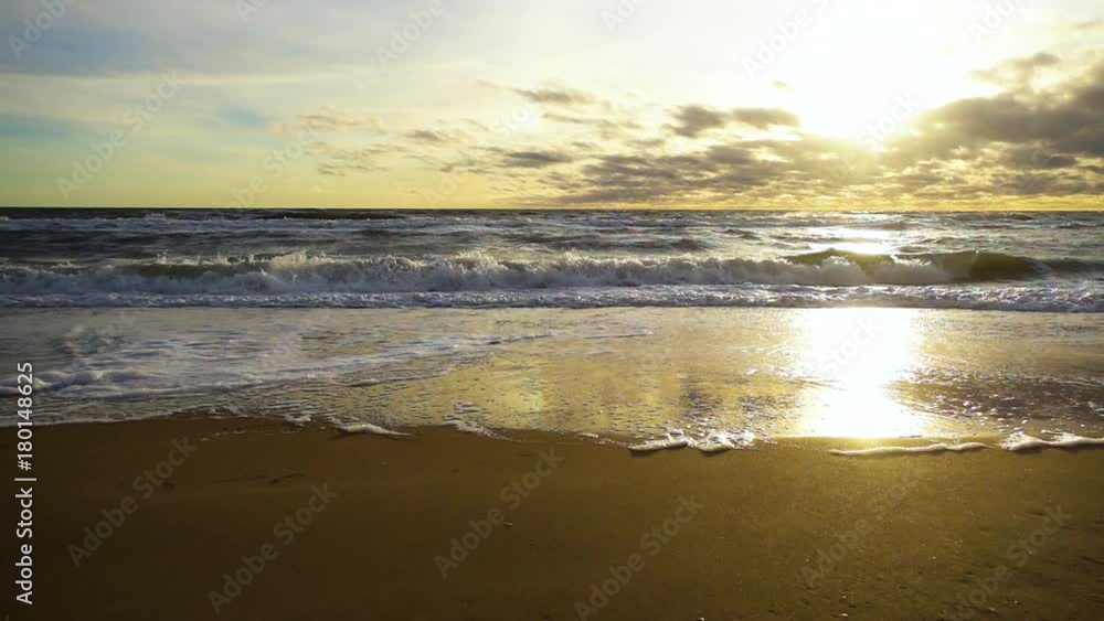 Slow mo among the clouds the sun shines brightly on the stormy sea with waves rushing to the sandy shore Slow mo among the clouds the sun shines brightly on the stormy sea with waves rushing to the sandy shore