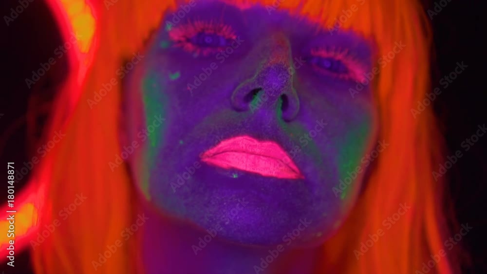 Closeup woman face with fluorescent make up and wig, creative makeup look great for nightclubs. Halloween party, shows and music concept - slow motion video Closeup woman face with fluorescent make up and wig, creative makeup look great for nightclubs. Halloween party, shows and music concept - slow motion video