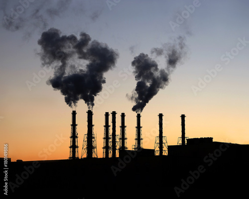 Industrial landscape with black silhouette of electric power station with many high smoke pipes in the evening after sunset over cloudless red and violet sky