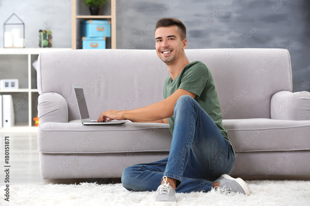 Obraz premium Young man with modern laptop near sofa at home