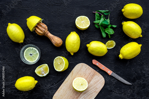 Make lemonade at home. Lemons, juicer, glass for beverage, knife, cutting board on black background top view