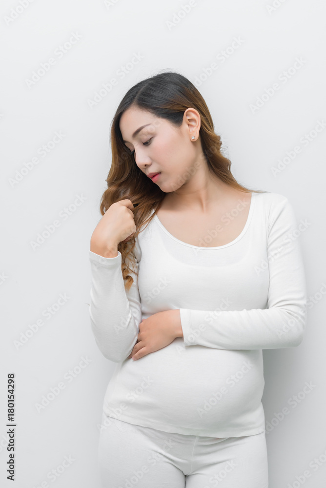 A pregnant woman in white dress standing holding her belly. A pregnant woman in white dress standing holding her belly.