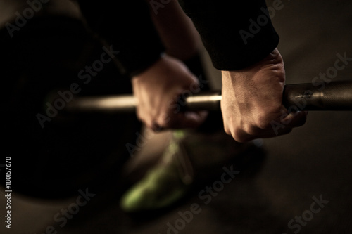 Close-up of a weight lifter in start position for sumo deadlift high pull, showing two hands on a barbell and a foot
