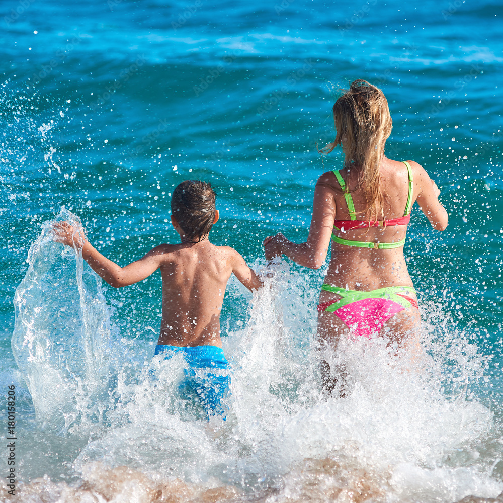 Caucasian mom and son running into the sea water. Back view. Caucasian mom and son running into the sea water. Back view.