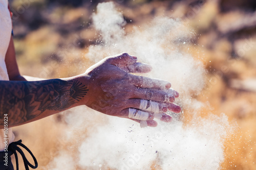Foto Dark skinned woman with arm tattoos and taped tingers claps her hands with chalk