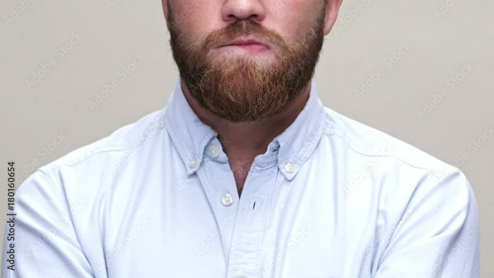 Cropped close up view of bearded man in shirt bites his lips over gray background Cropped close up view of bearded man in shirt bites his lips over gray background