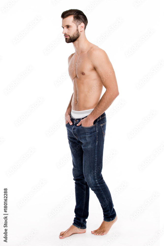 Casual and shirtless. Full length of handsome young man in jeans looking away while standing against white background. Casual and shirtless. Full length of handsome young man in jeans looking away while standing against white background.
