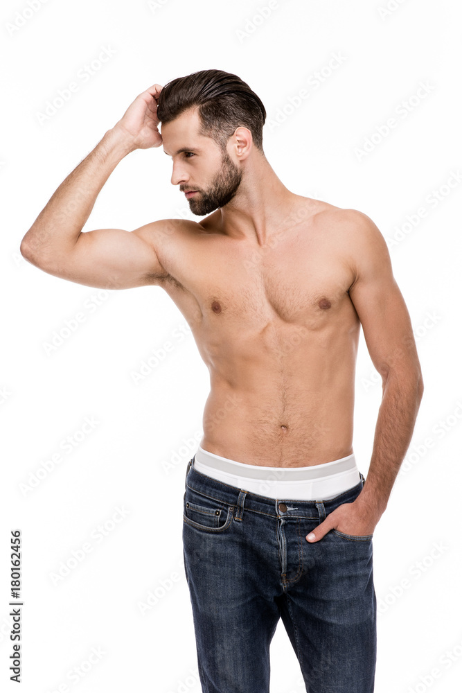 Stunning and handsome. Handsome shirtless young man in jeans looking away while standing against white background Stunning and handsome. Handsome shirtless young man in jeans looking away while standing against white background