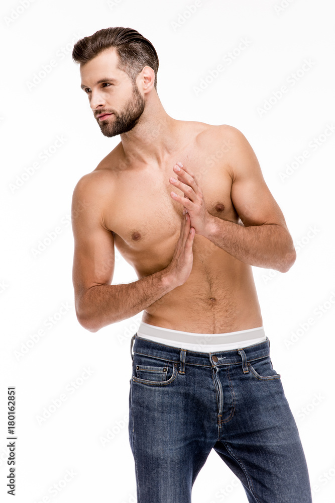 Gorgeous and handsome. Handsome shirtless young man in jeans looking away while standing against white background