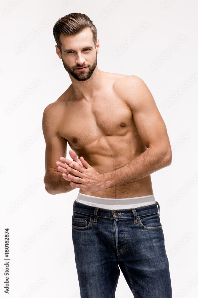 Fototapeta premium Gorgeous torso. Handsome shirtless young man in jeans looking at camera while standing against white background