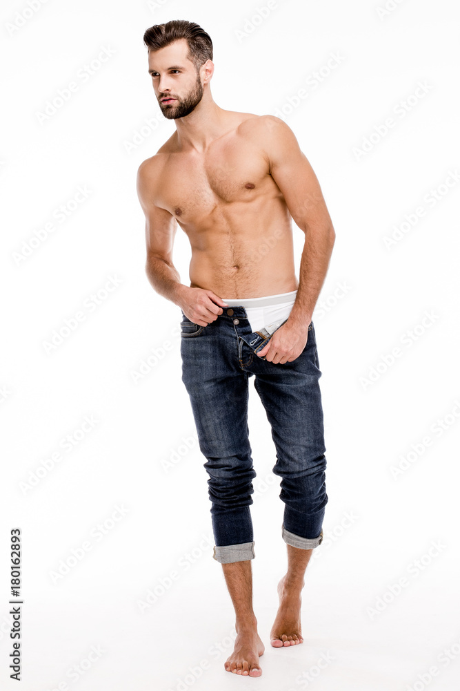 Casual handsome man. Full length of handsome shirtless young man taking off his jeans while standing against white background. Casual handsome man. Full length of handsome shirtless young man taking off his jeans while standing against white background.