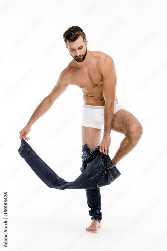 Taking off that jeans. Full length of handsome shirtless young man taking off his jeans and looking away while standing against white background. Taking off that jeans. Full length of handsome shirtless young man taking off his jeans and looking away while standing against white background.