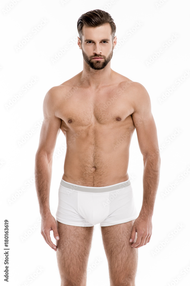 Confident and sexy. Handsome shirtless young man in white pants looking at camera while standing against white background. Confident and sexy. Handsome shirtless young man in white pants looking at camera while standing against white background.