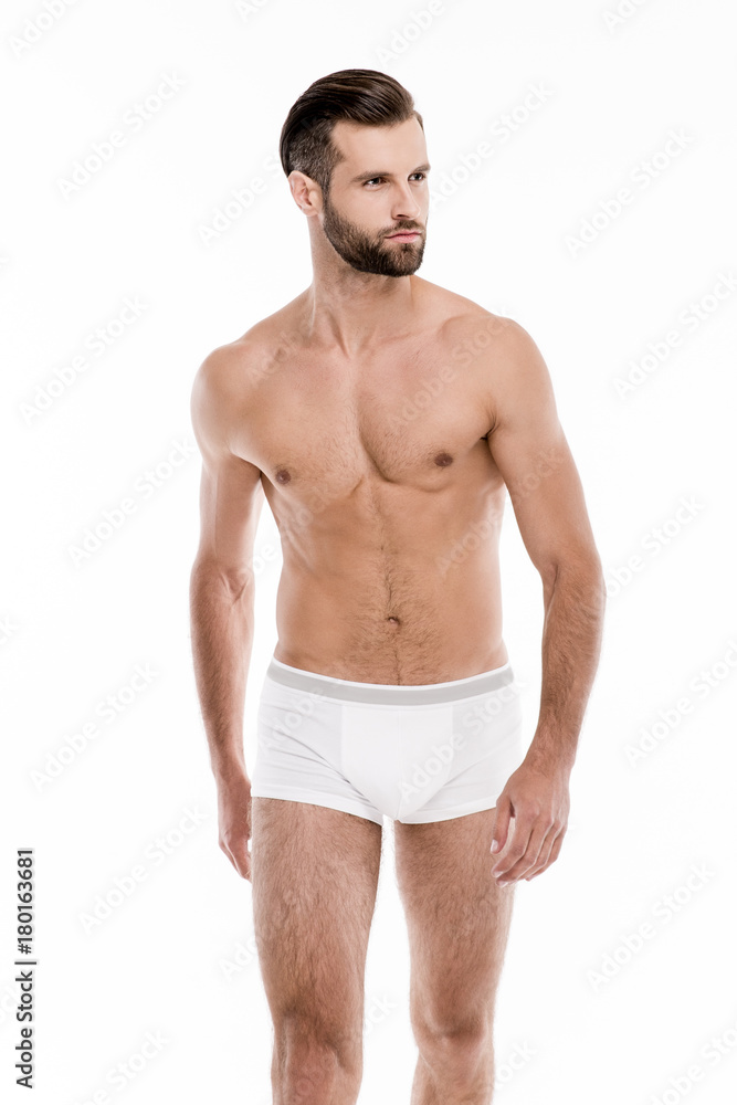Muscular and healthy. Handsome shirtless young man in white pants looking away while standing against white background. Muscular and healthy. Handsome shirtless young man in white pants looking away while standing against white background.
