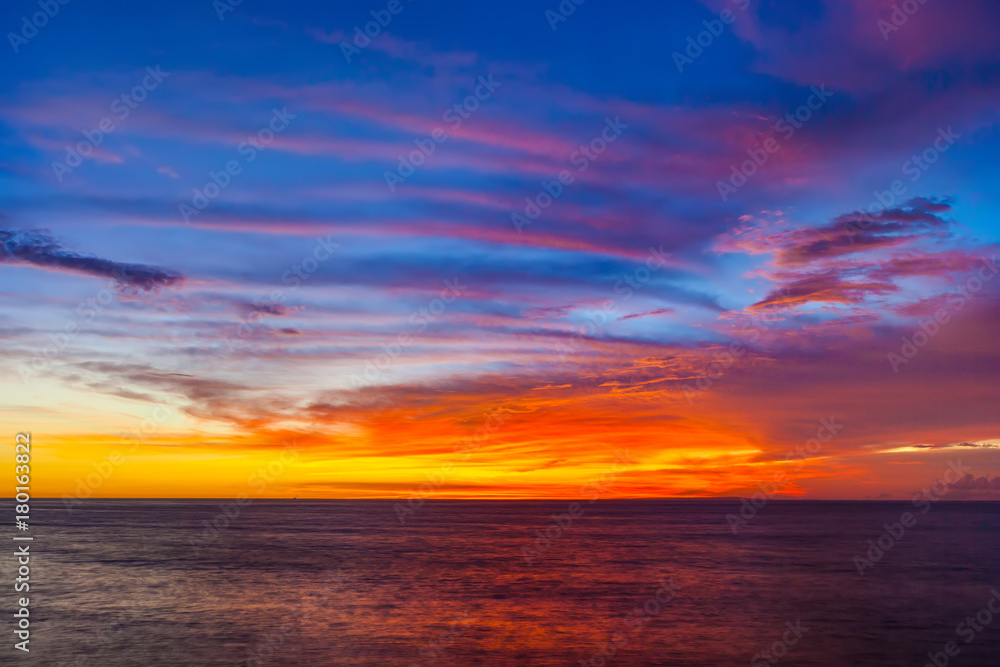 Stunning colorful sunset, blue sky, yellow purple cirrus clouds, orange sun, dark sea. Sunset on Jimbaran, South Kuta, Bali, Indonesia.