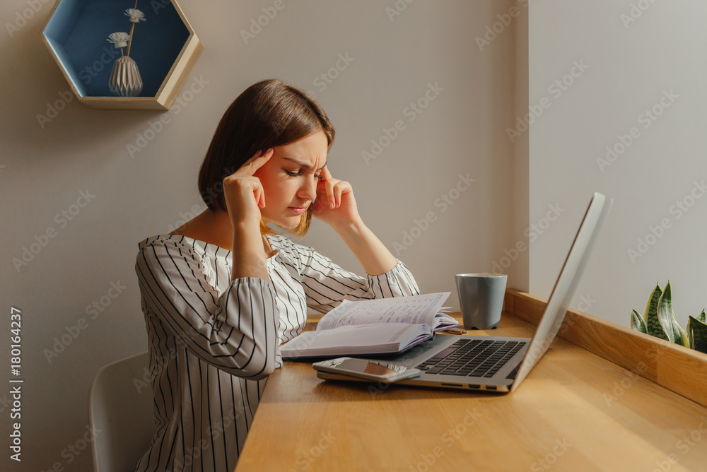 Young freelance girl worker sitting at cafe shop with phone, note book, laptop and thinking about work. Freelance work place.