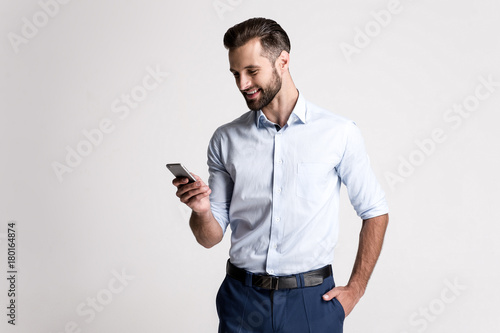 Great email! Handsome young man using his phone with smile while standing against white background.