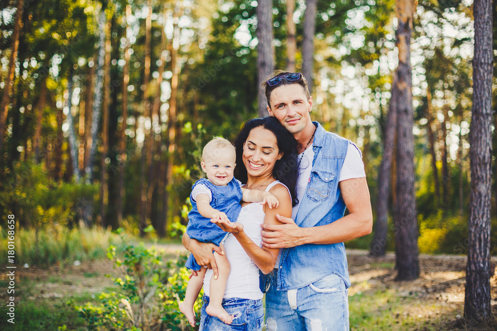 Obraz premium stylish beautiful fashionable parents are holding a girl in the park on the background of a dense forest.