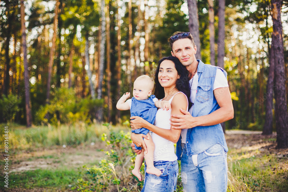 Fototapeta premium stylish beautiful fashionable parents are holding a girl in the park on the background of a dense forest.