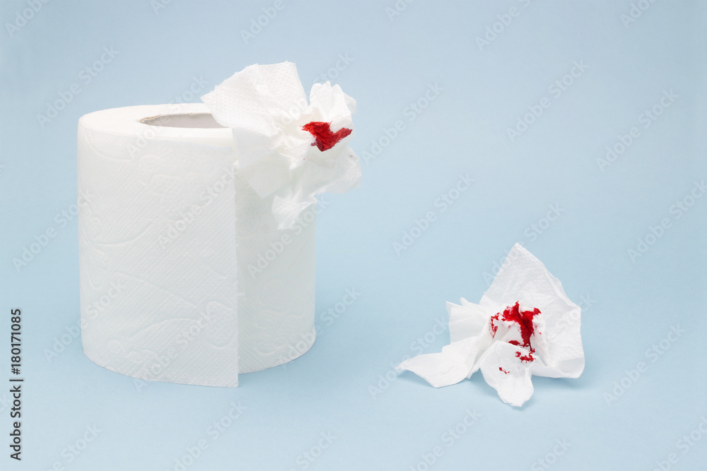 A photo of a toilet paper roll and two used bloody toilet paper sheets. Blood drops and traces