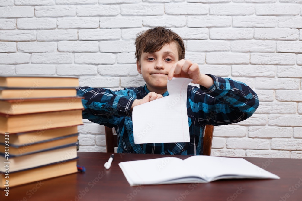 Stressed and exhausted schoolboy tearing papers sitting at the desk