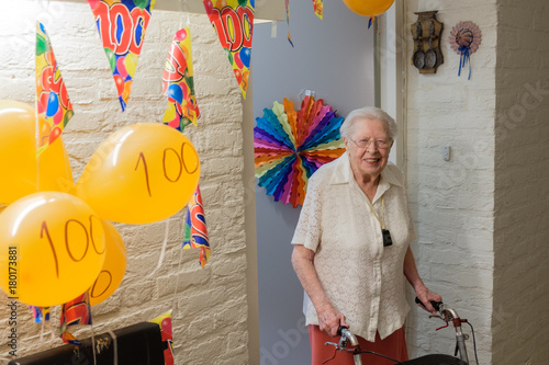 senior woman stands in front of her decorated room door celebrating her 100th birthday