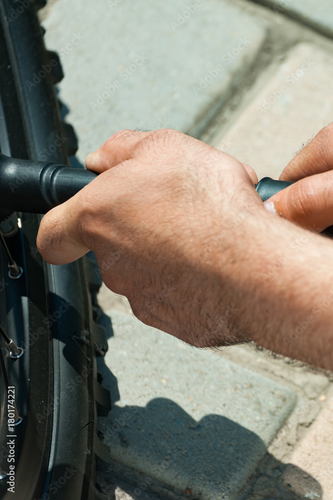 Side and vertical view of man pumping bicycle tyre outdoors, close-up of hands