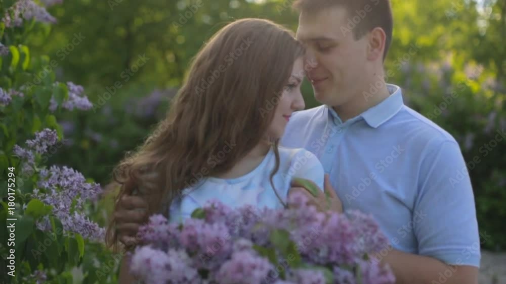 Loving guy and girl with a bouquet of lilac in the summer garden at sunset Loving guy and girl with a bouquet of lilac in the summer garden at sunset