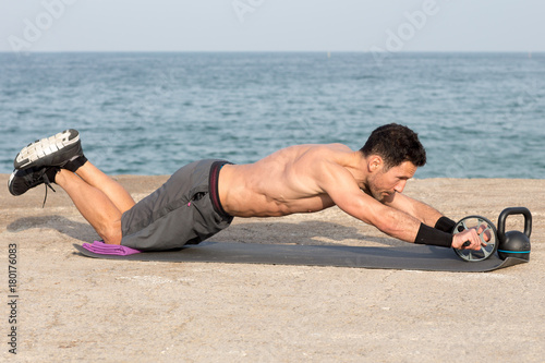 Athletic man during abdominal exercise by wheel training at seaside waterfront