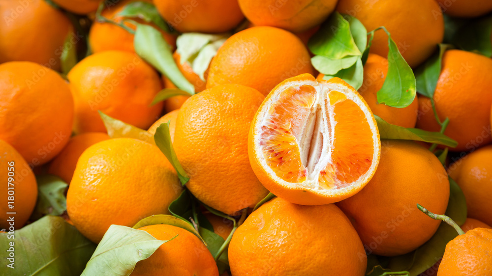 Citrus fruits background. Fresh tangerines oranges on market. Group of freshly picked oranges with their leaves forming a background. Top view of slices, whole of orange fruits and leaves close up. Citrus fruits background. Fresh tangerines oranges on market. Group of freshly picked oranges with their leaves forming a background. Top view of slices, whole of orange fruits and leaves close up.