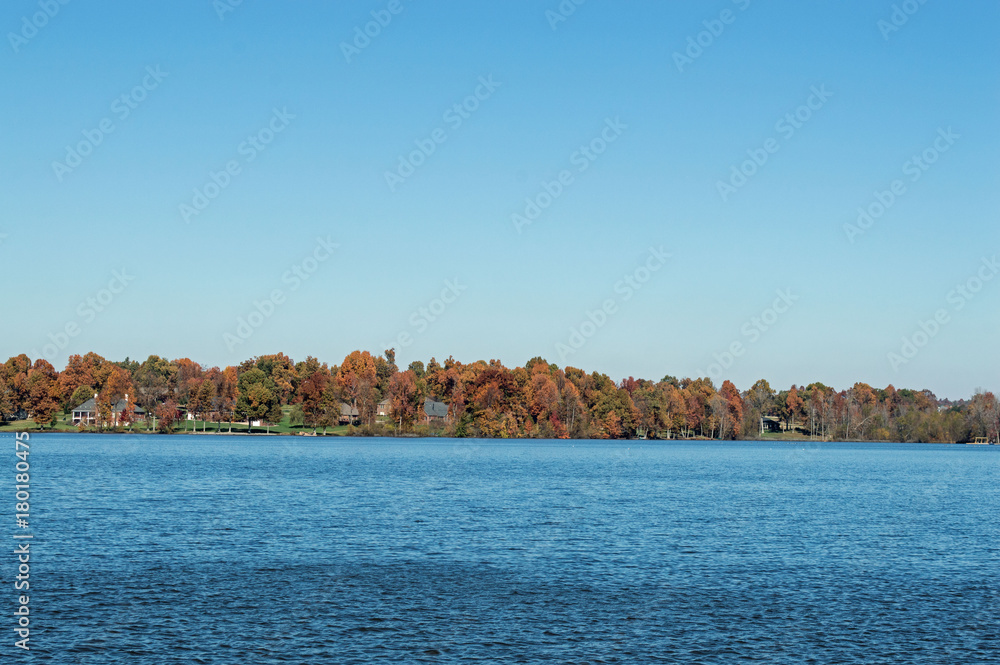 Landscape photo of a small lake lined with trees bearing autumn colors