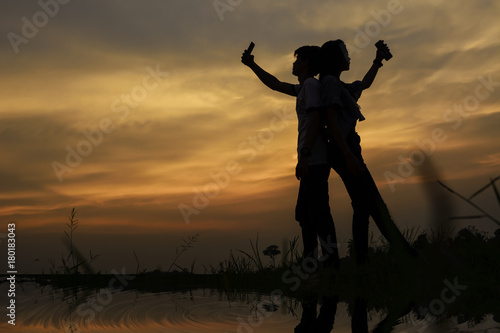 silhouette of a couple standing selfie on the riverside, have meadow on scary sky.