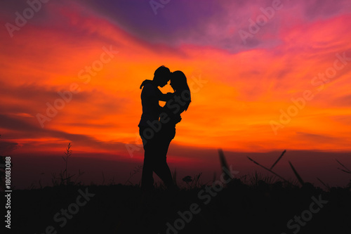 Fototapeta silhouette of romantic couple stand hugging on meadow at the sunset time