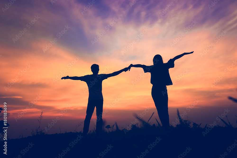 Fototapeta premium Couple holding hands with arms outstretched at sunset