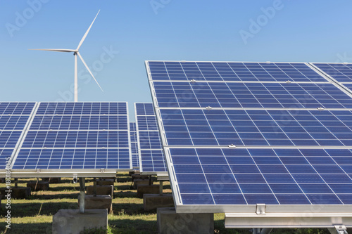  Rows array of polycrystalline silicon solar panels and wind turbines generating electricity in hybrid power plant systems station 