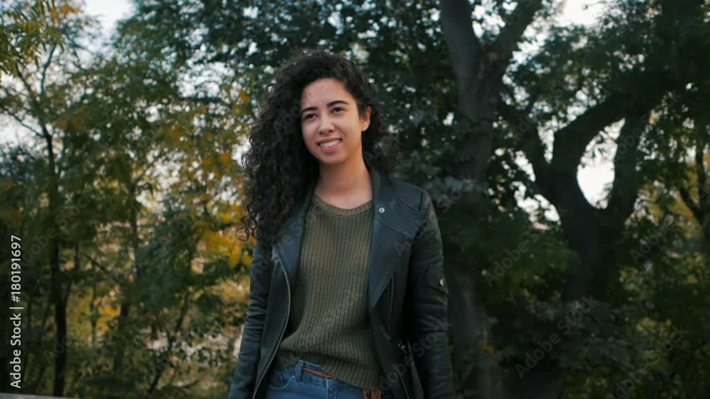 Portrait of happy young woman with beautiful curly hair in the street, slow motion. Hispanic girl smiling to camera Portrait of happy young woman with beautiful curly hair in the street, slow motion. Hispanic girl smiling to camera