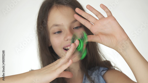 Beautiful cheerful teen girl playing with green fidget spinner on white background