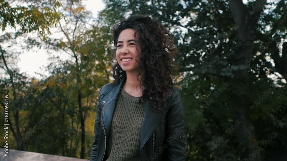 Portrait of happy young woman with beautiful curly hair in the street, slow motion. Hispanic girl smiling to camera Portrait of happy young woman with beautiful curly hair in the street, slow motion. Hispanic girl smiling to camera