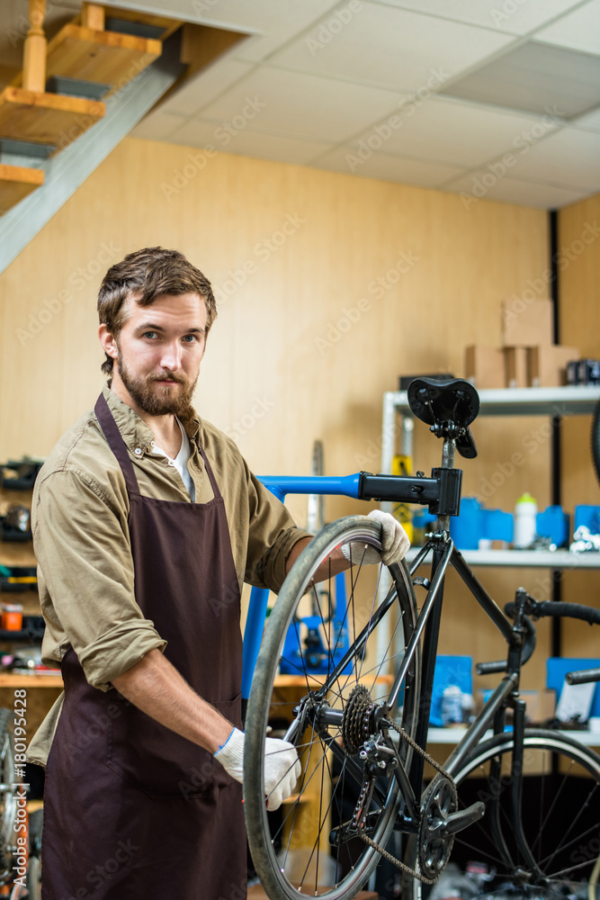 Confident repairman in uniform tightening gear of bicycle wheel