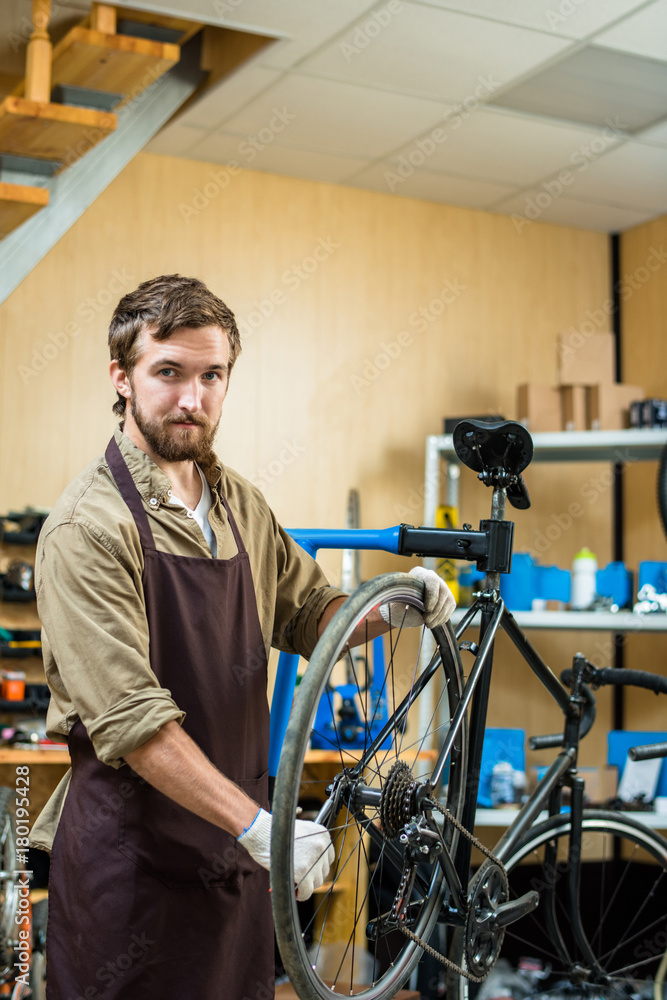 Confident repairman in uniform tightening gear of bicycle wheel Confident repairman in uniform tightening gear of bicycle wheel