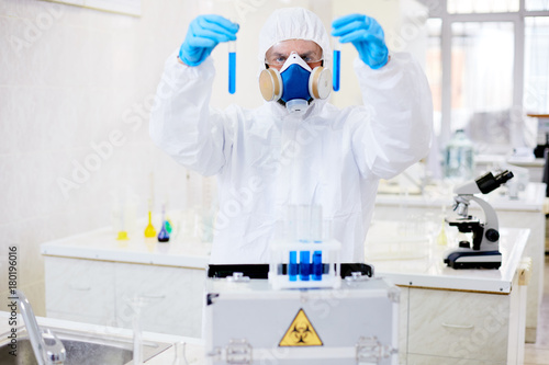 Scientist in protective clothes comparing two toxic liquids in lab