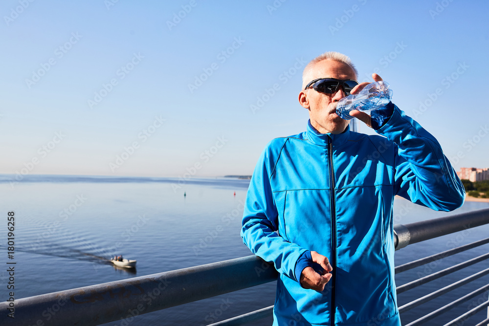 Sporty mature man drinking fresh water from plastic bottle after workout