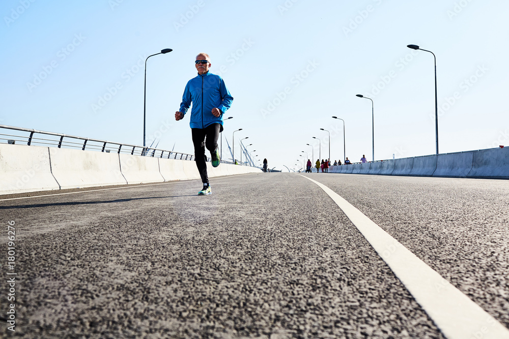 Active sportsman running down urban road on sunny morning