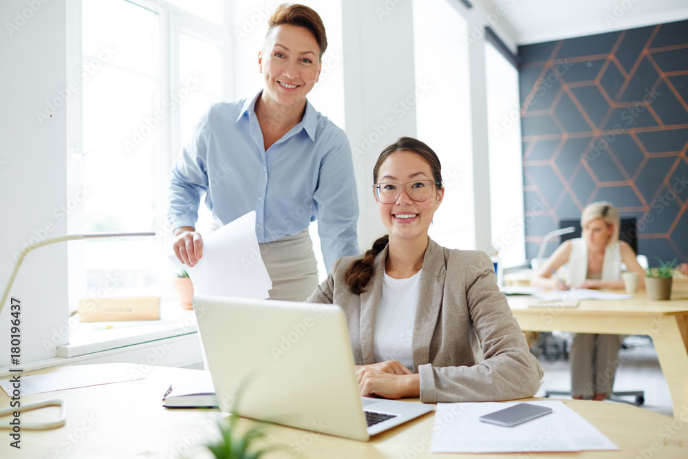 Successful young women looking at camera by their workplace in studio Successful young women looking at camera by their workplace in studio