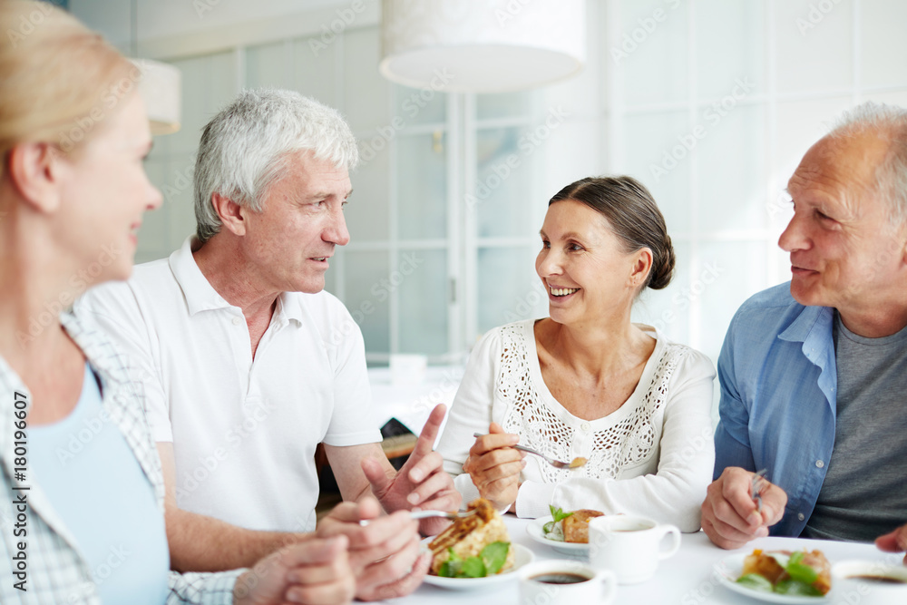 Friendly senior people gathered by table having talk by dessert with tea Friendly senior people gathered by table having talk by dessert with tea