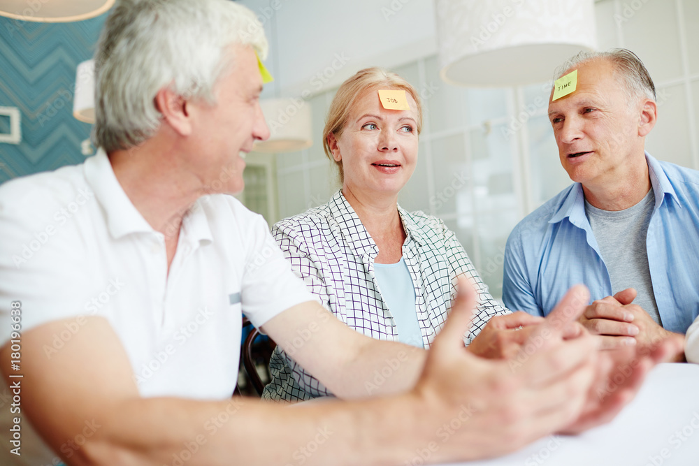 Senior people brainstorming while guessing characters on notepaper stuck on their foreheads Senior people brainstorming while guessing characters on notepaper stuck on their foreheads